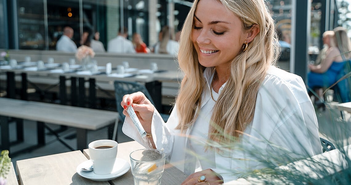 Donna bionda con camicia bianca che mescola The Solution nel caffè